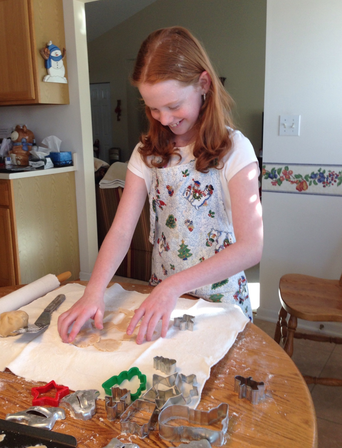 Young Elizabeth in a holiday apron cutting out cookie shapes in the kitchen